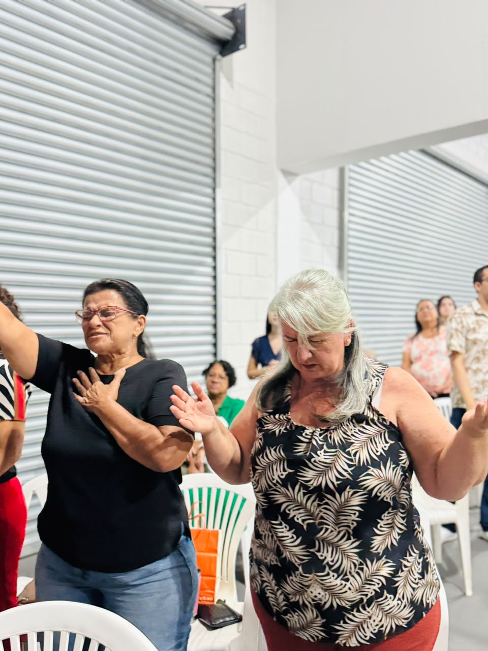 Duas mulheres em profunda adoração, de olhos fechados e mãos sobre o peito, durante o culto.