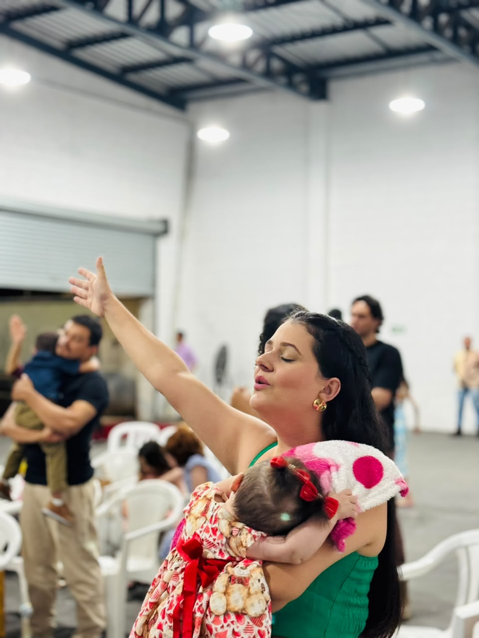 Mãe segurando seu bebê no colo enquanto adora a Deus com a mão levantada.